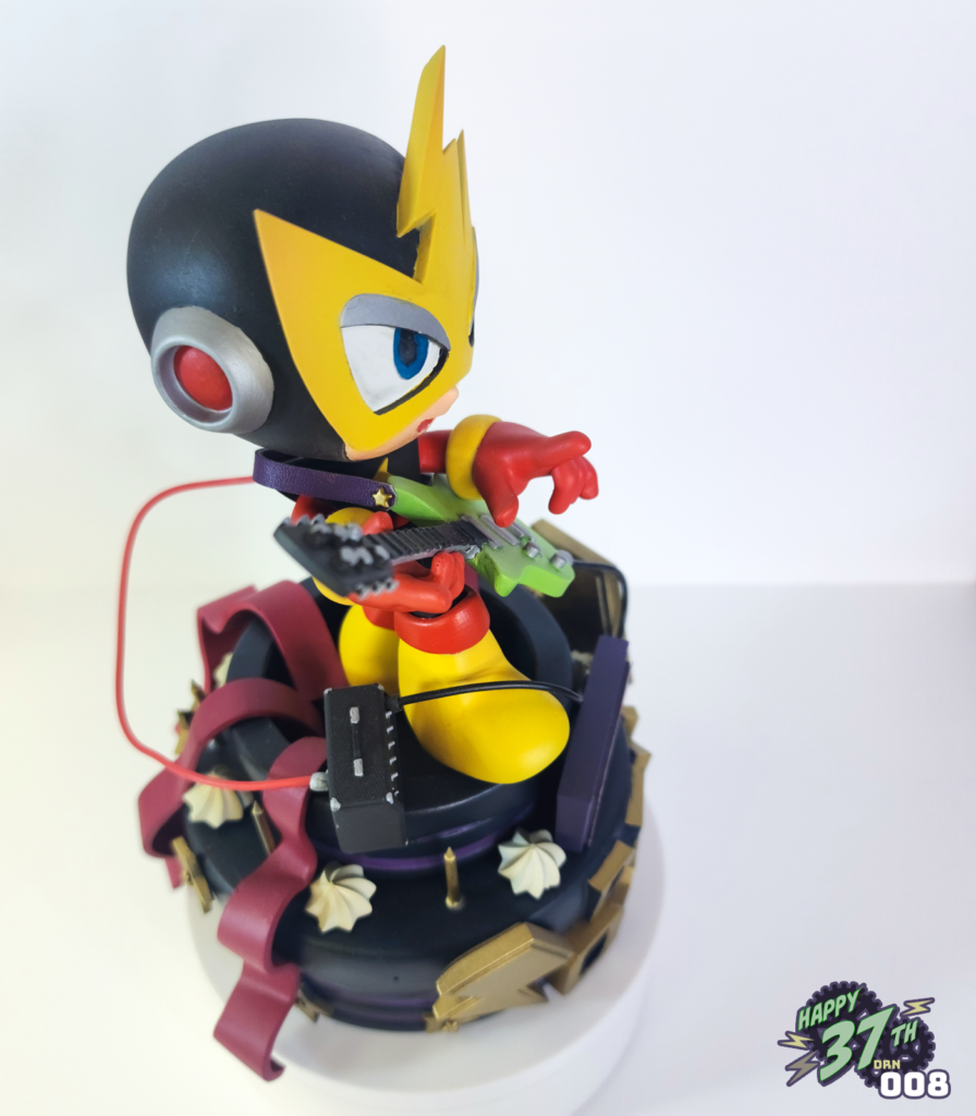 Side view of fan figure depicting Elecman standing on a purple and black cake while playing guitar