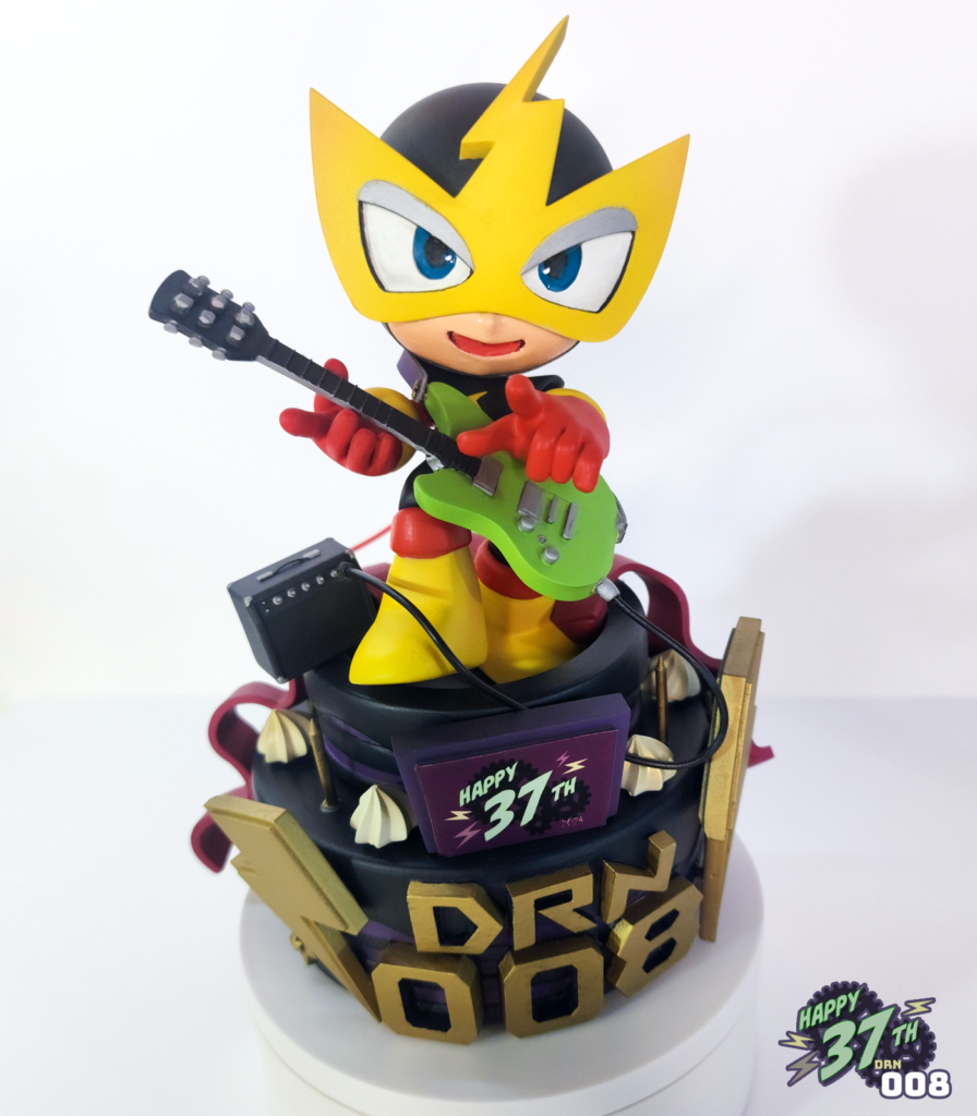 Front view of fan figure depicting Elecman standing on a purple and black cake while playing guitar